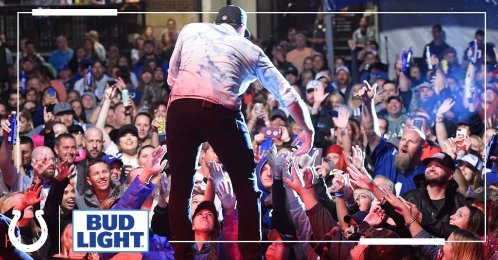 artist singing on stage leaning over to grab hand of audience member, colts logo, bud light logo