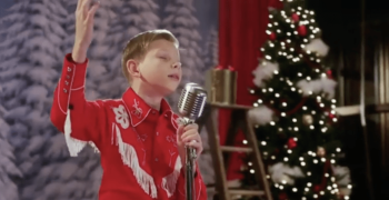 Mason Ramsey singing on stage and Christmas trees in the background