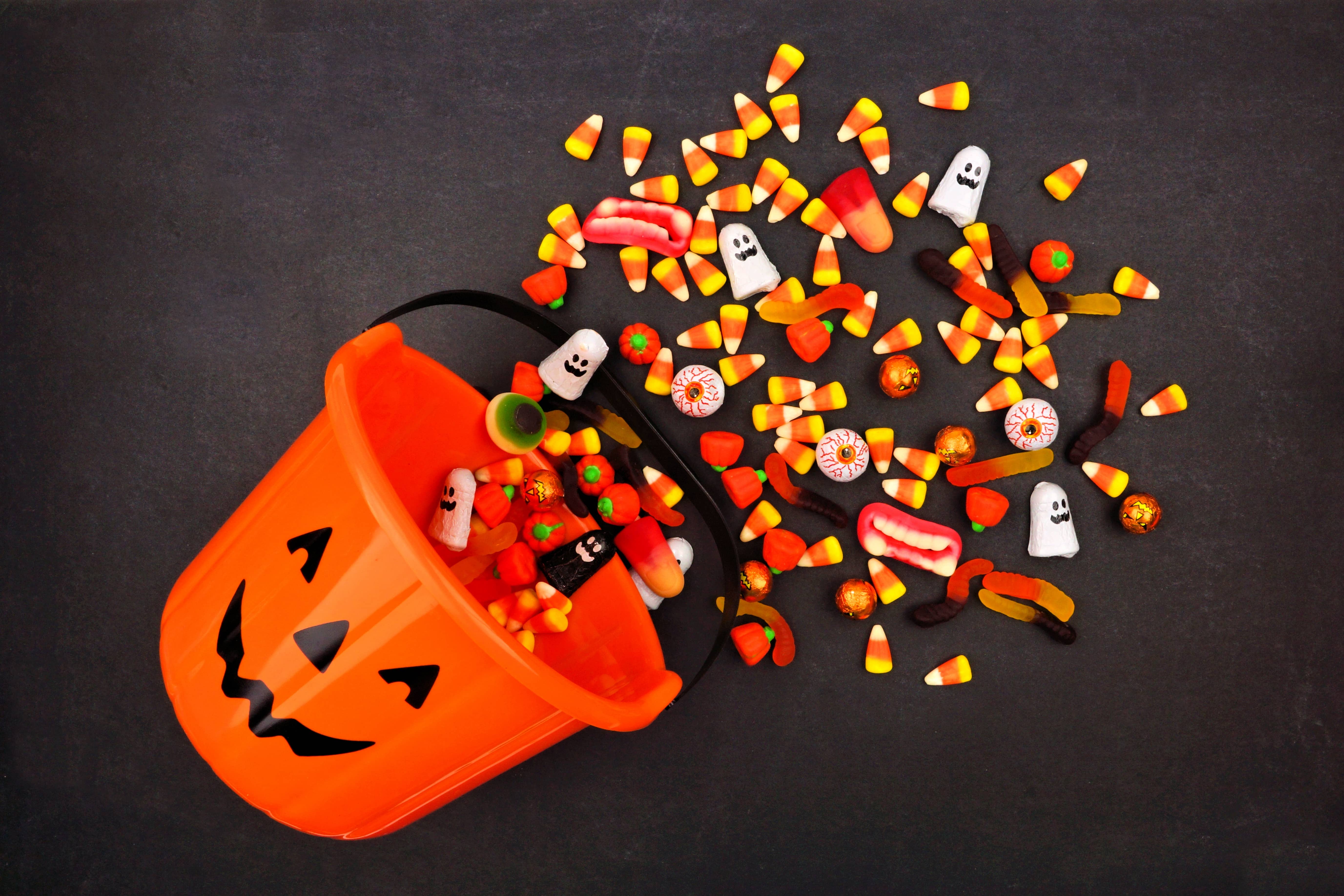 Halloween Jack o Lantern pail with spilling candy, above view on a dark background