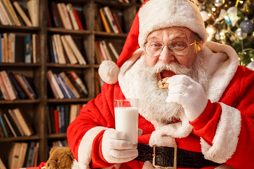 Santa Claus in the library holding glass of milk and eating a cookie