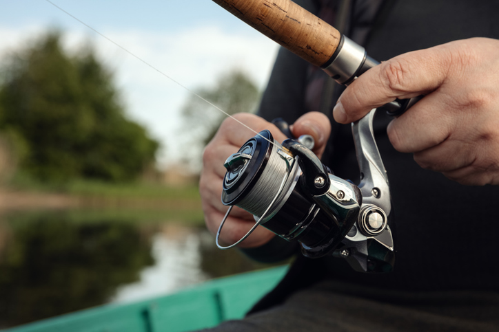 Freshwater fishing in summer. Spinning reel on a spinning rod in the hands of a fisherman.