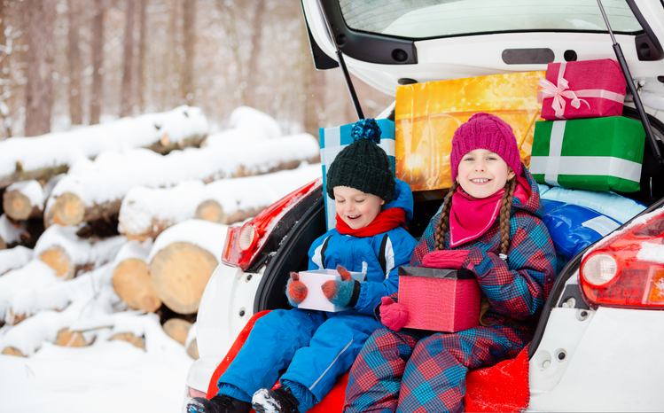 Merry Christmas. Happy New Year. Happy family children sitting in car loaded with boxes of gifts and Christmas tree against the background of forest in snowy weather.