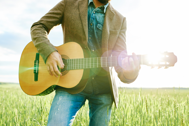 Young Adult Caucasian Man Playing Acoustic Guitar Outdoors in Sunlit Field
