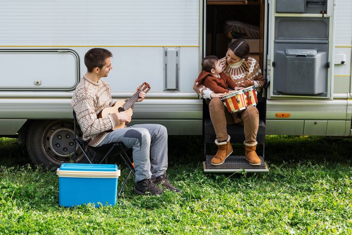 Woman teaching her baby to play the drums with her husband camping in a caravan.